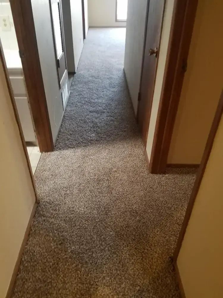 Narrow carpeted hallway with wooden door frames and a bright room at the far end