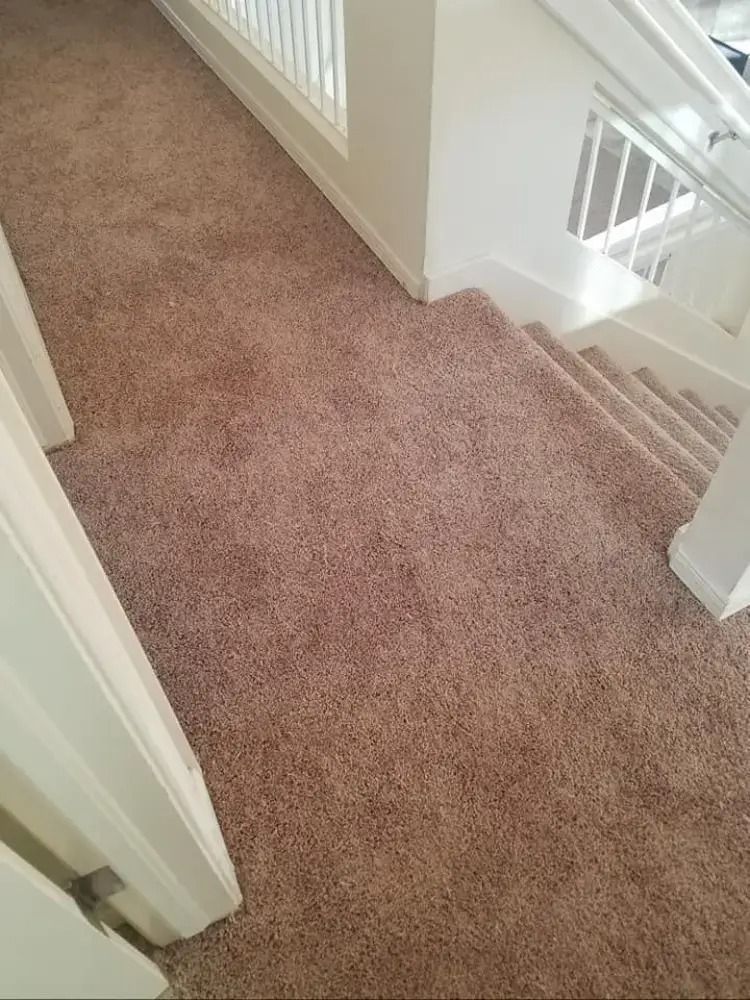 Carpeted upstairs hallway beside a staircase with white railings and walls