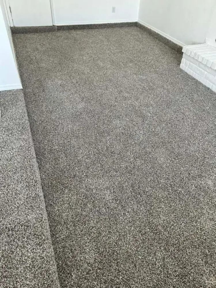 Empty gray carpeted room with white walls and baseboards