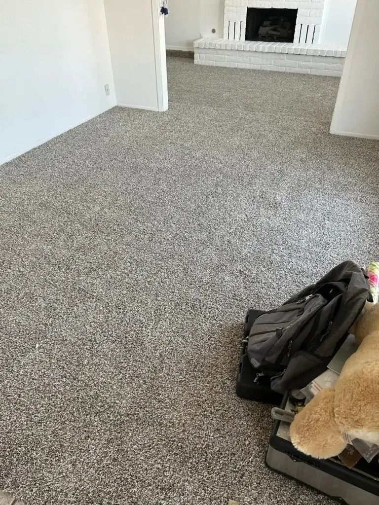 Empty carpeted living room with a fireplace in the background and a backpack on the floor in the foreground