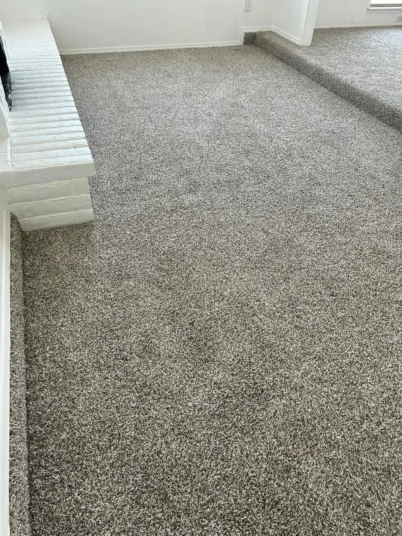 Empty gray carpeted room with white walls and a stacked pile of white bricks along the left side