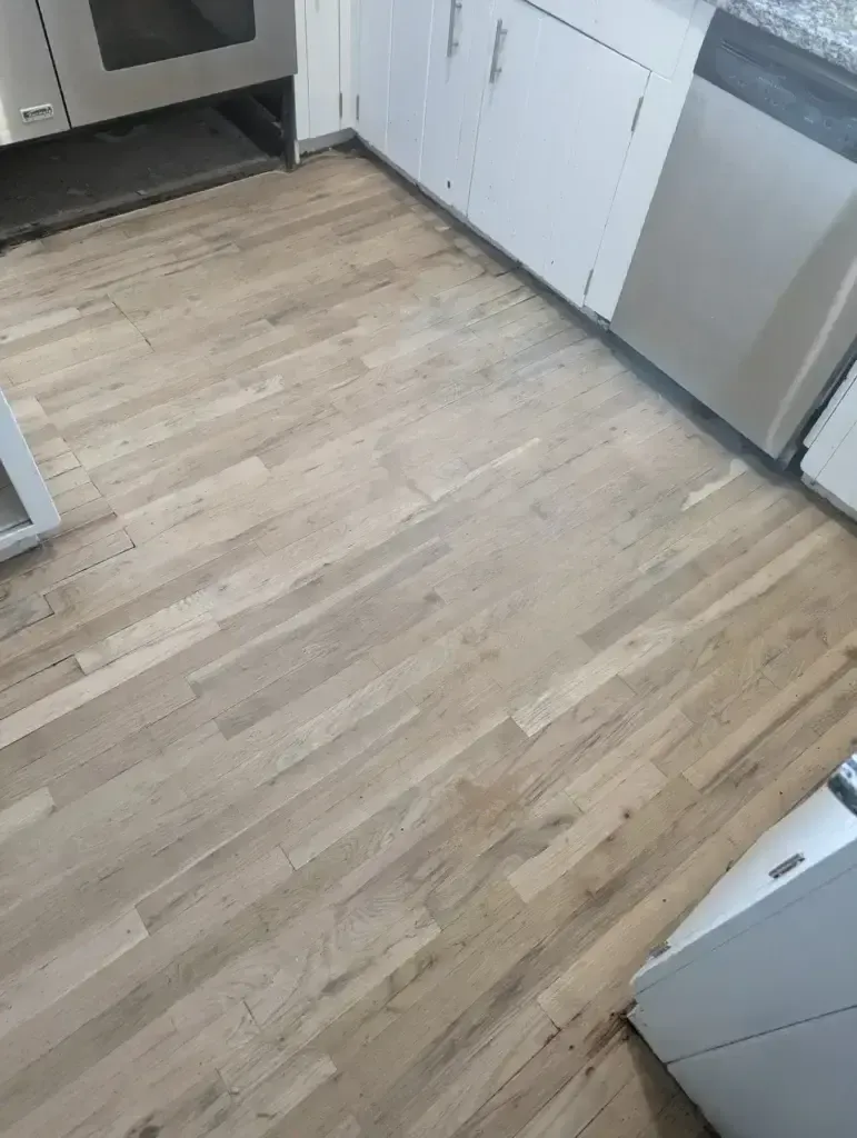 Empty kitchen with light wood floor and white cabinets, viewed from the doorway.