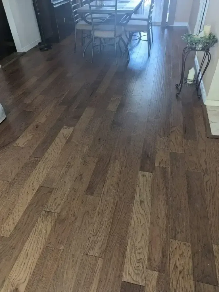 Wooden hallway floor leading to a dining area with chairs and a small plant stand on the right