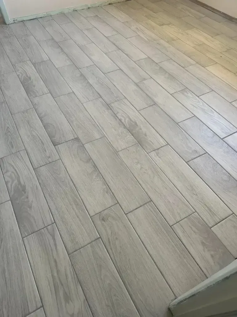 Light wood-look tile floor in a bright room, with part of a white wall and doorway visible.