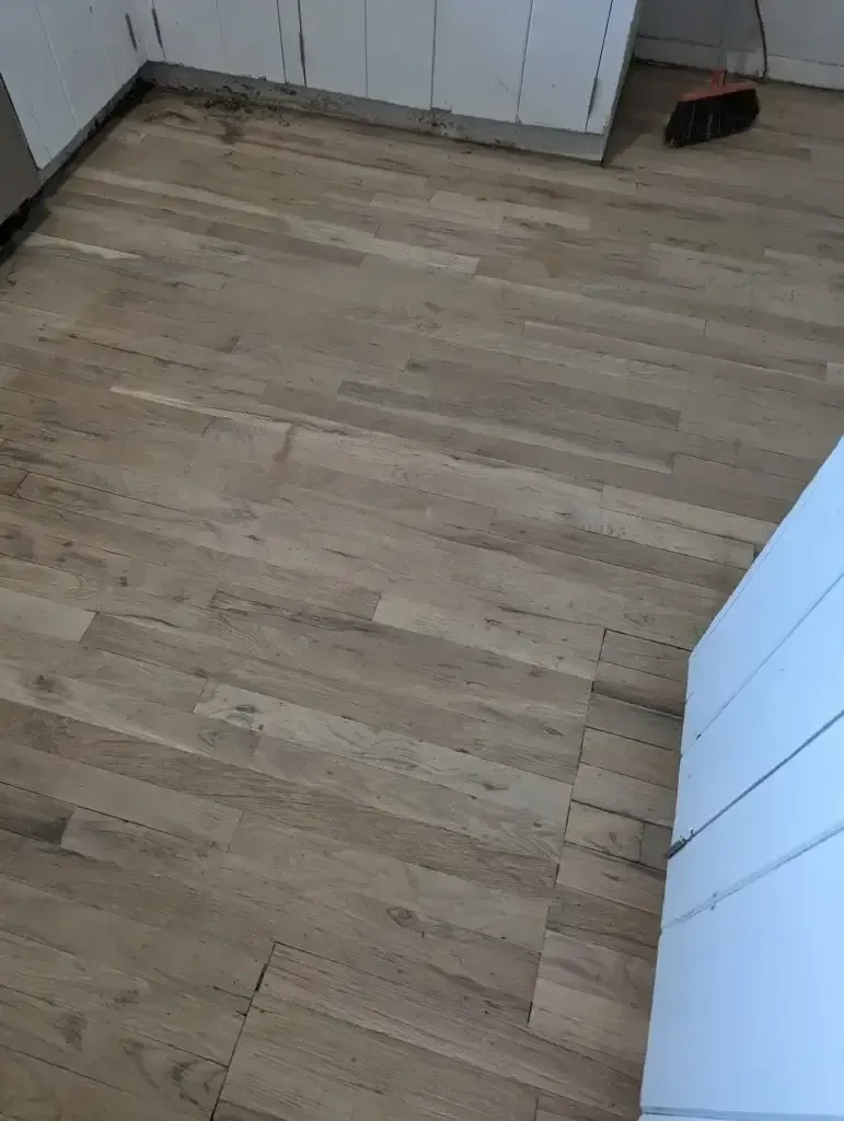 Empty room with light wood flooring and white cabinets along one wall.