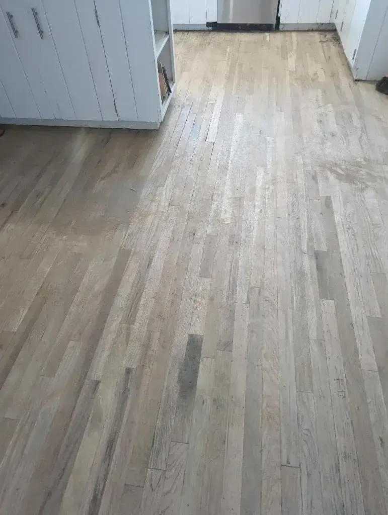 Empty hallway with worn light wood flooring and white cabinets along the left wall