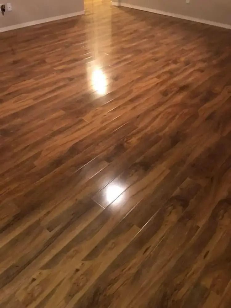 Empty room with glossy wooden floor and white walls, reflecting light.