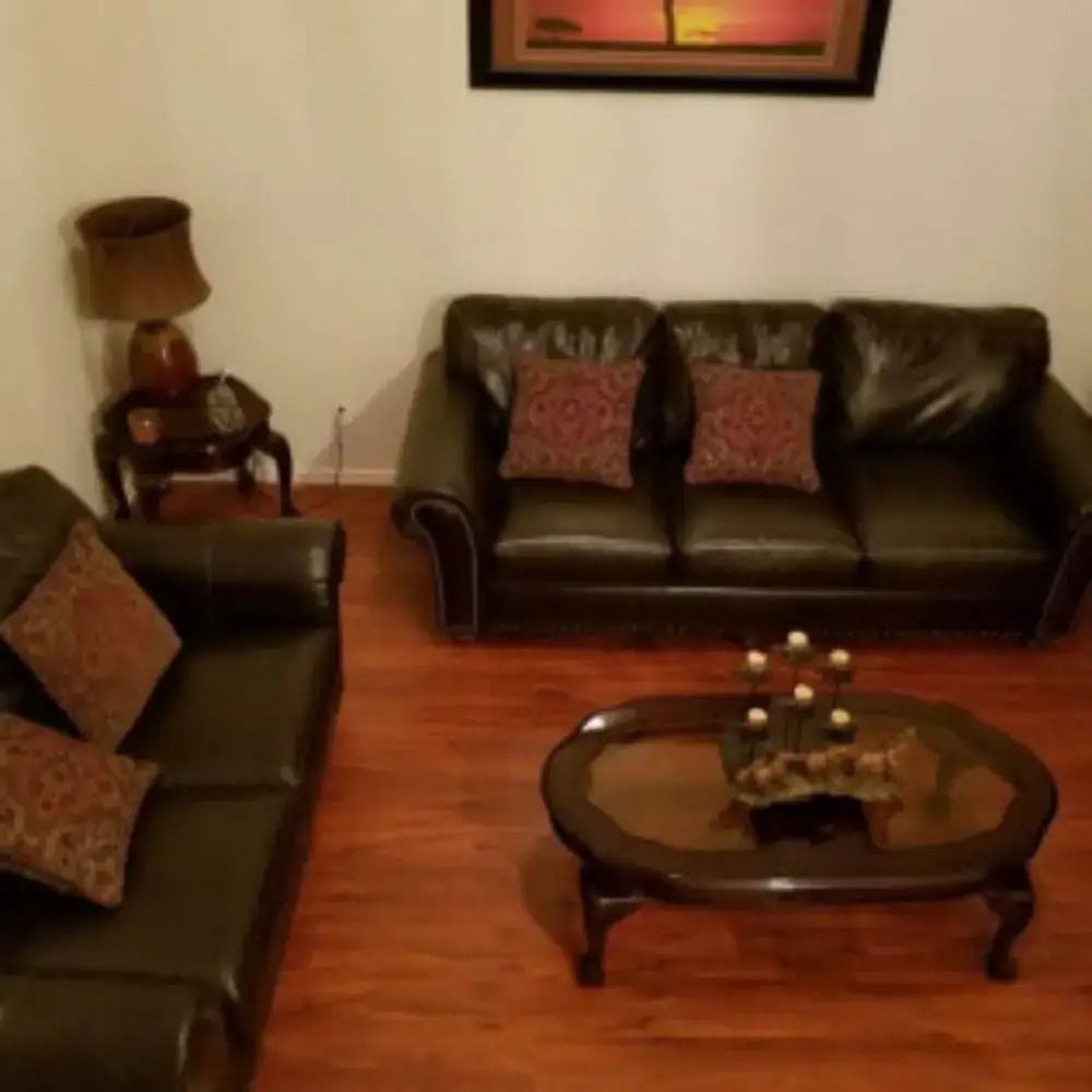 Cozy living room with two dark leather sofas, a glass coffee table, and warm wooden flooring.