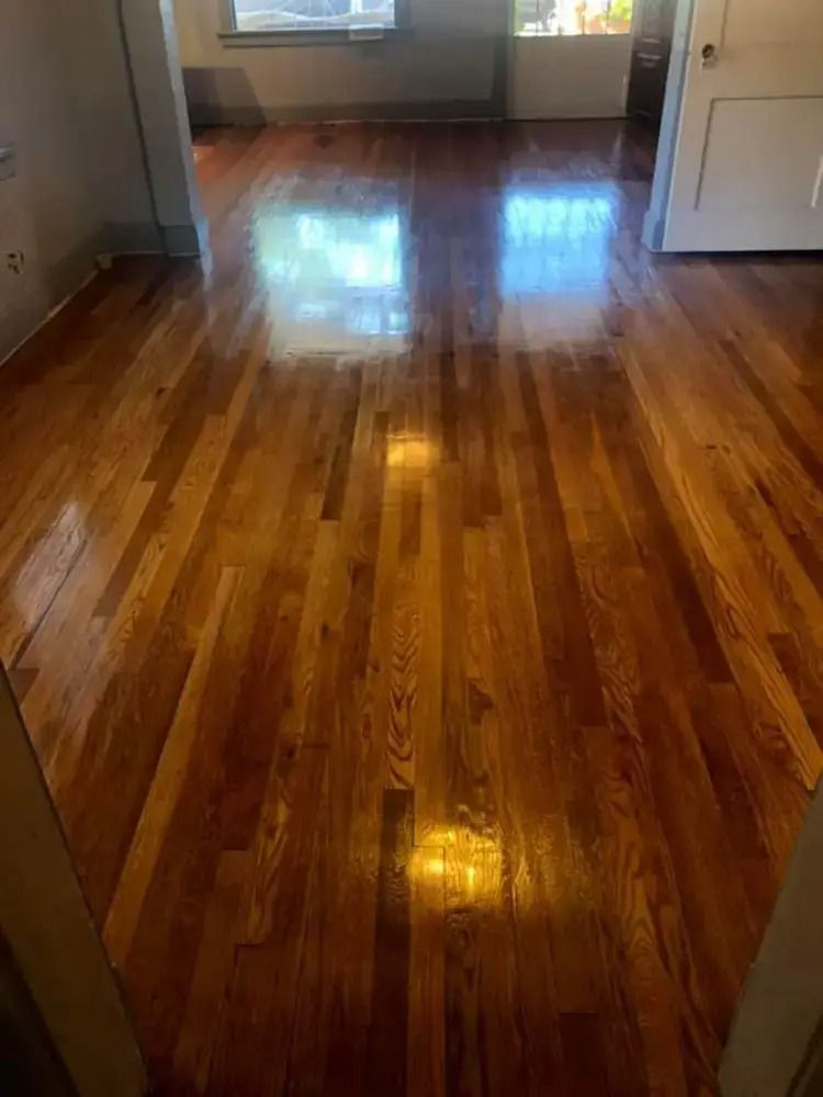 Shiny hardwood floor in an empty room with sunlight reflections and a window at the far end