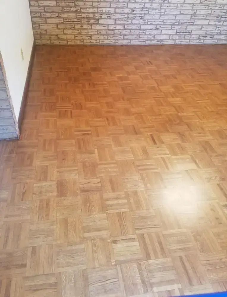 Empty room with parquet wood floor, white walls, and a brick-patterned back wall.
