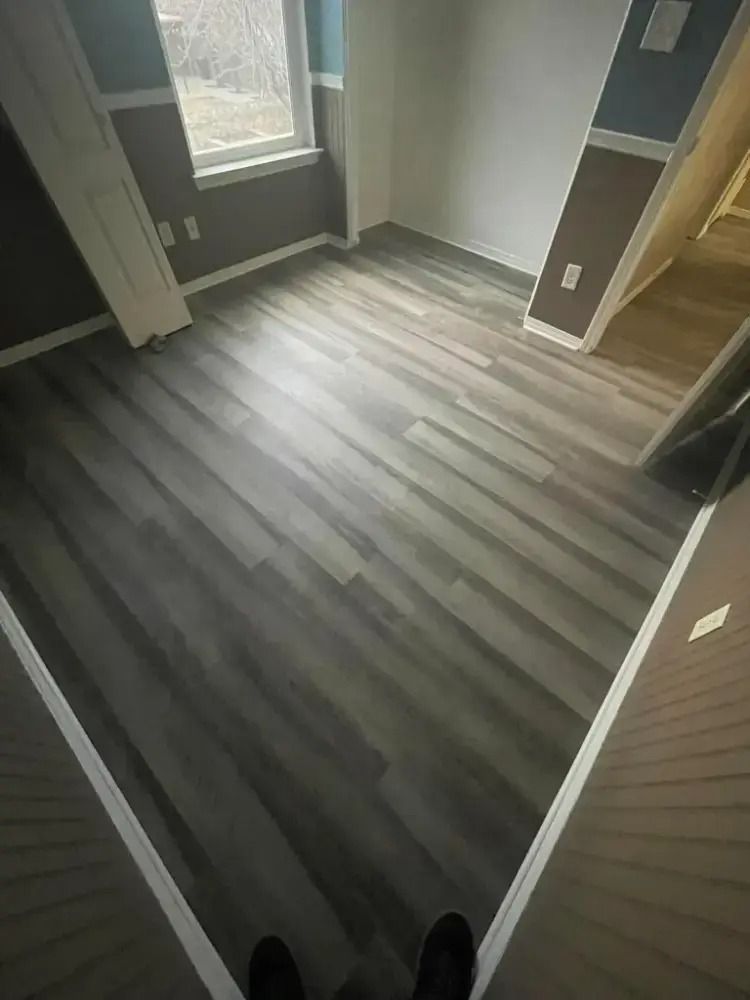 Empty room with gray wood-look flooring, gray walls, a window, and an open doorway to the right
