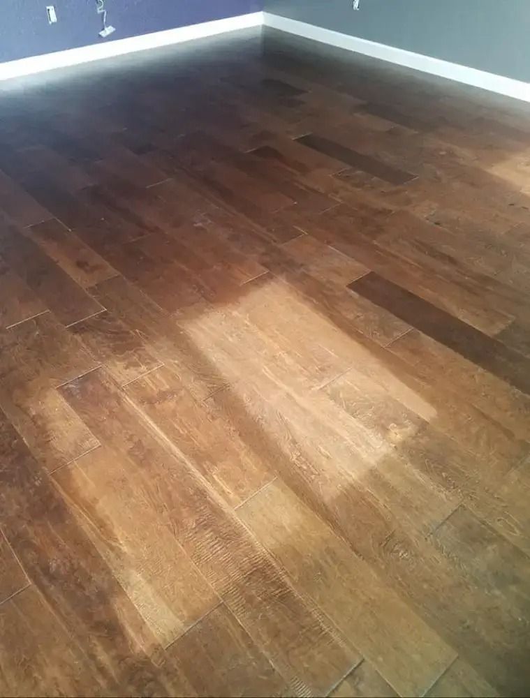 Empty room corner with dark wood flooring and gray walls, lit by sunlight near the window