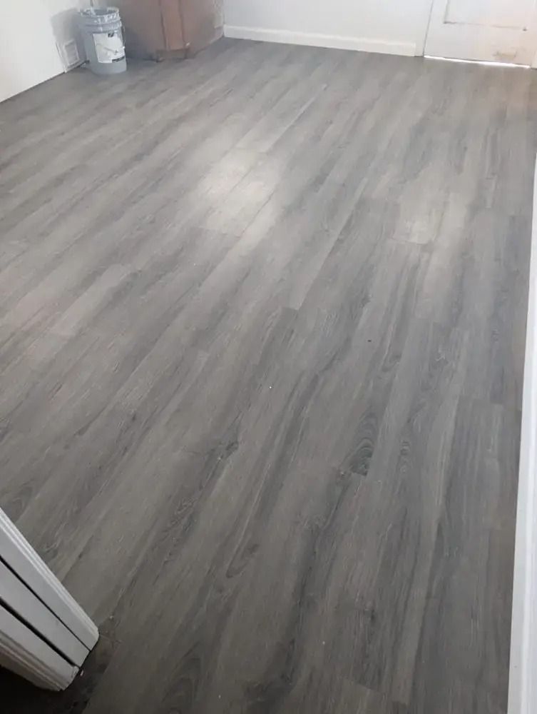 Empty room with gray wood-look flooring and white walls, viewed from the doorway.