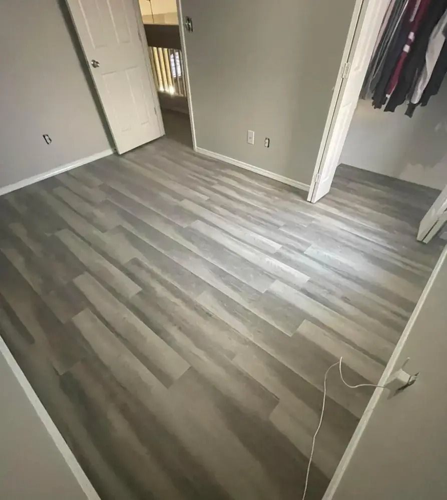 Empty room with gray wood flooring, open closet, and white walls.