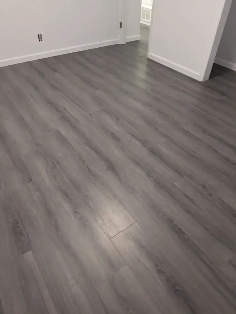 Empty room with gray wood flooring and white walls, viewed from a corner.