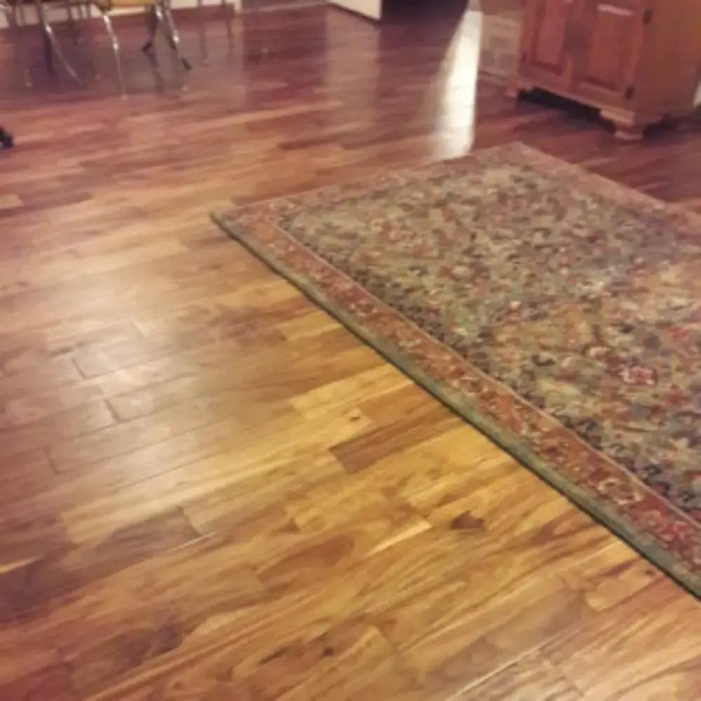 Wooden floor beside a patterned rug in a room with dining chairs and a cabinet