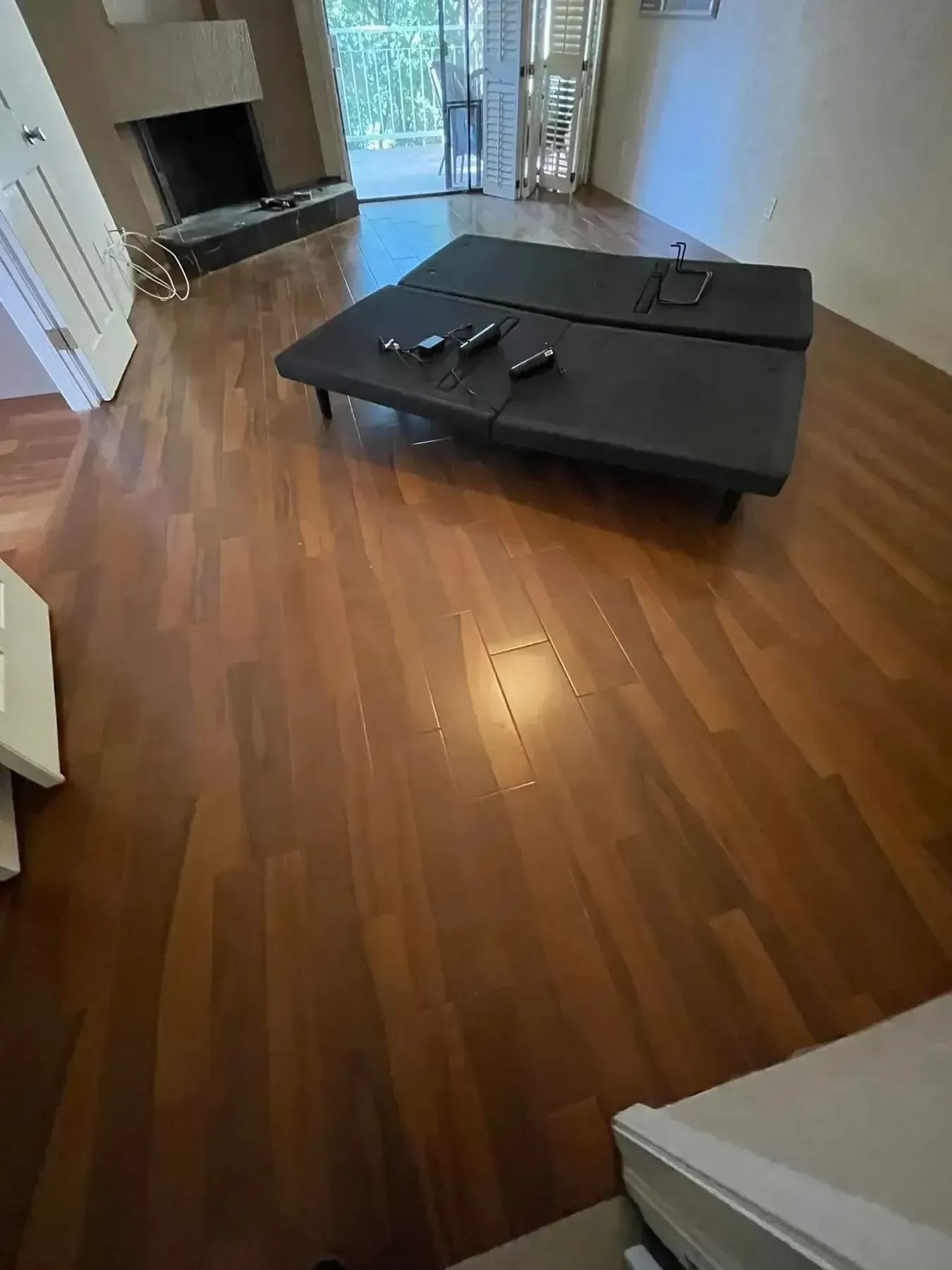 Empty living room with hardwood floors and a black sectional sofa near a fireplace and sliding glass doors