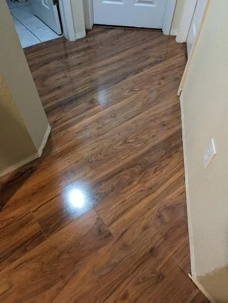 Hallway with glossy wood-look flooring and beige walls, leading to closed doors.