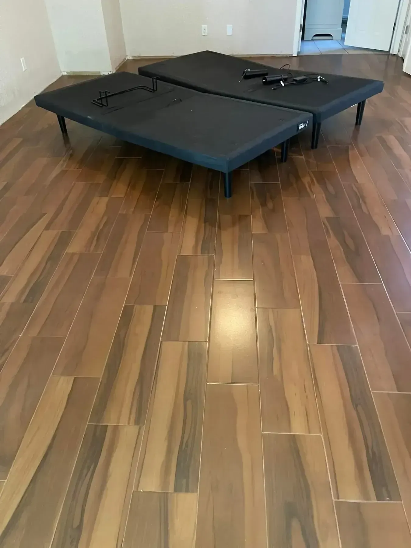 Two black foldable beds on a wood floor in a sparsely furnished room.