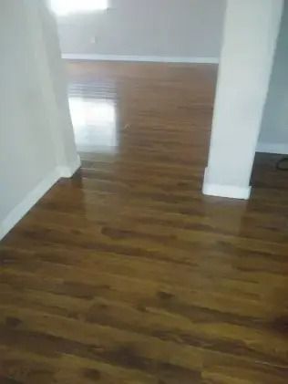 Empty room with polished hardwood floors and white walls, viewed through a doorway.