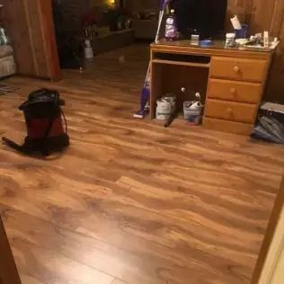 Wooden-floored room with a desk, drawers, and a vacuum cleaner in the foreground.