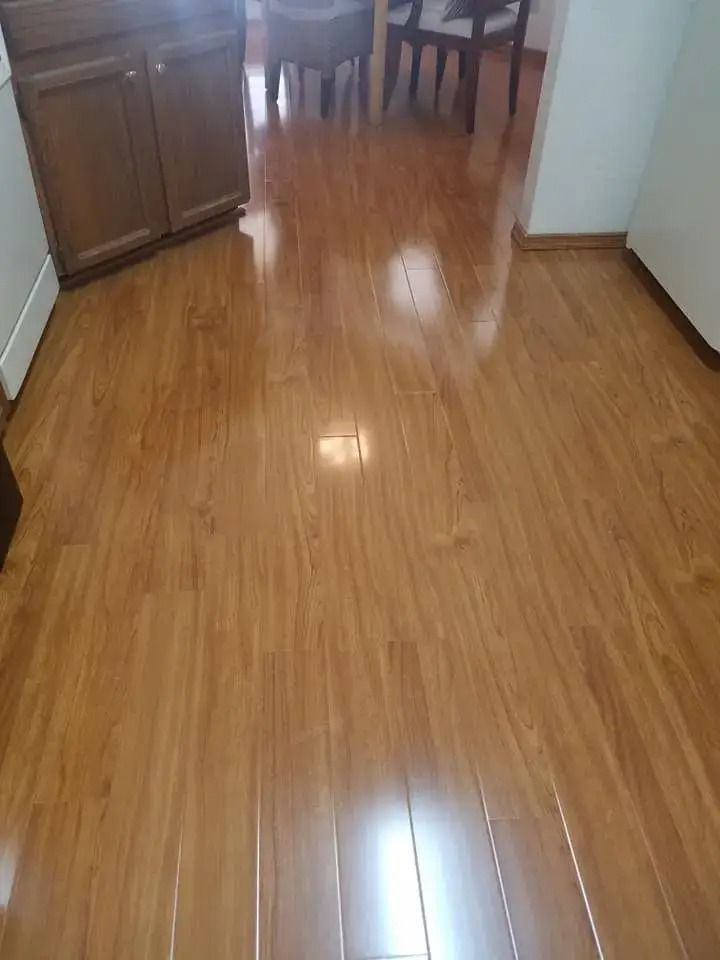 Shiny hardwood floor in a home hallway with wood cabinets and dining chairs in the background
