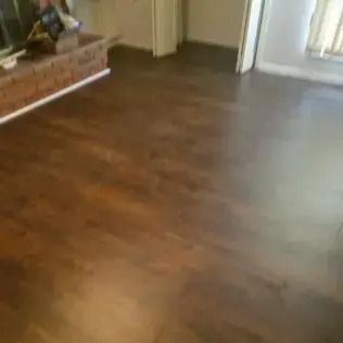 Empty room with dark wood flooring and a brick fireplace on the left.