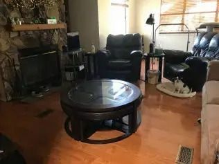 Cozy living room with dark leather chairs, round coffee table, fireplace, and warm wood floor.