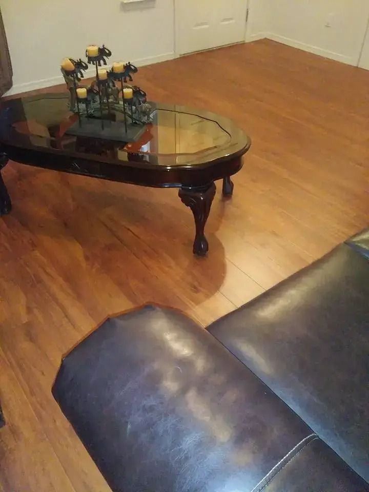 Living room with glass coffee table, toy model on top, wood floor, and black leather sofa edge