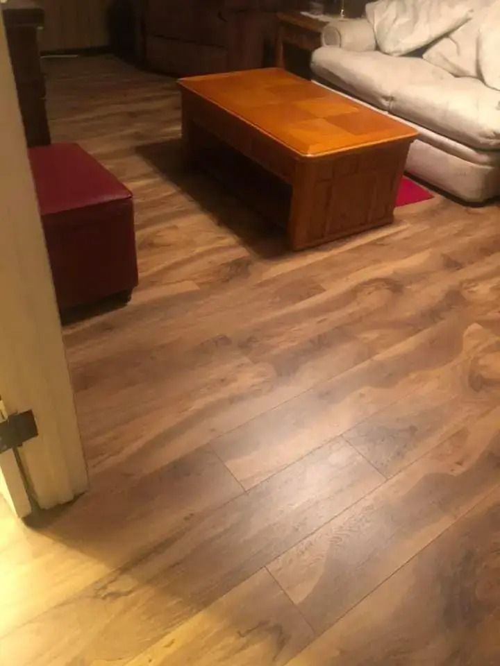 Living room with wood flooring, a wooden coffee table, and a beige sofa with a red ottoman nearby.