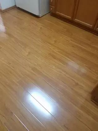 Shiny hardwood kitchen floor with light reflections and wooden cabinets in the corner
