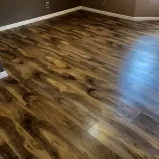 Empty room with glossy wood-look flooring and brown walls, lit by natural light.