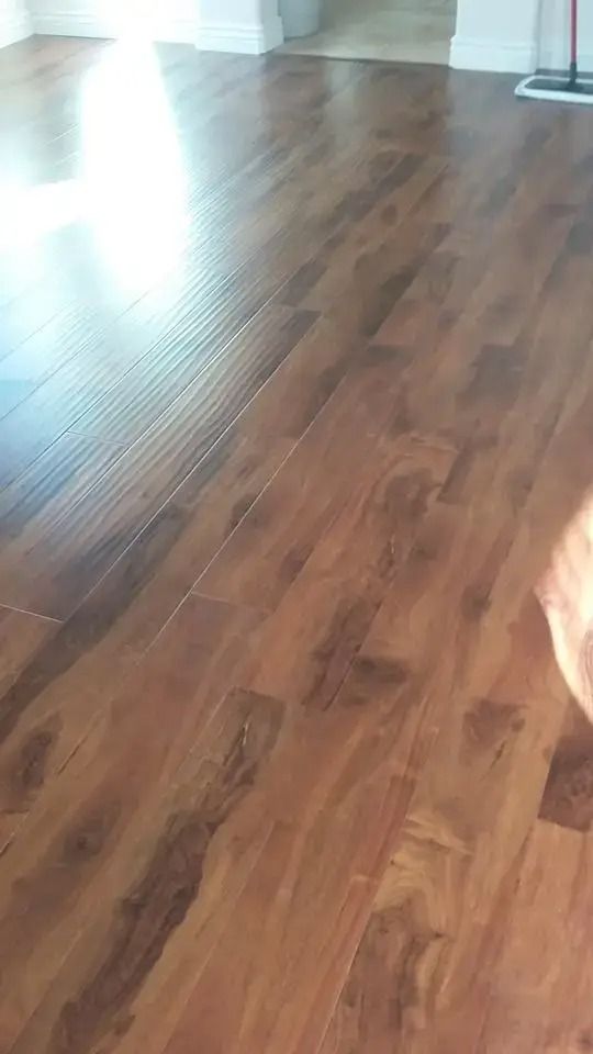 Sunlit wooden floor in an empty room, with reflections and a doorway in the background