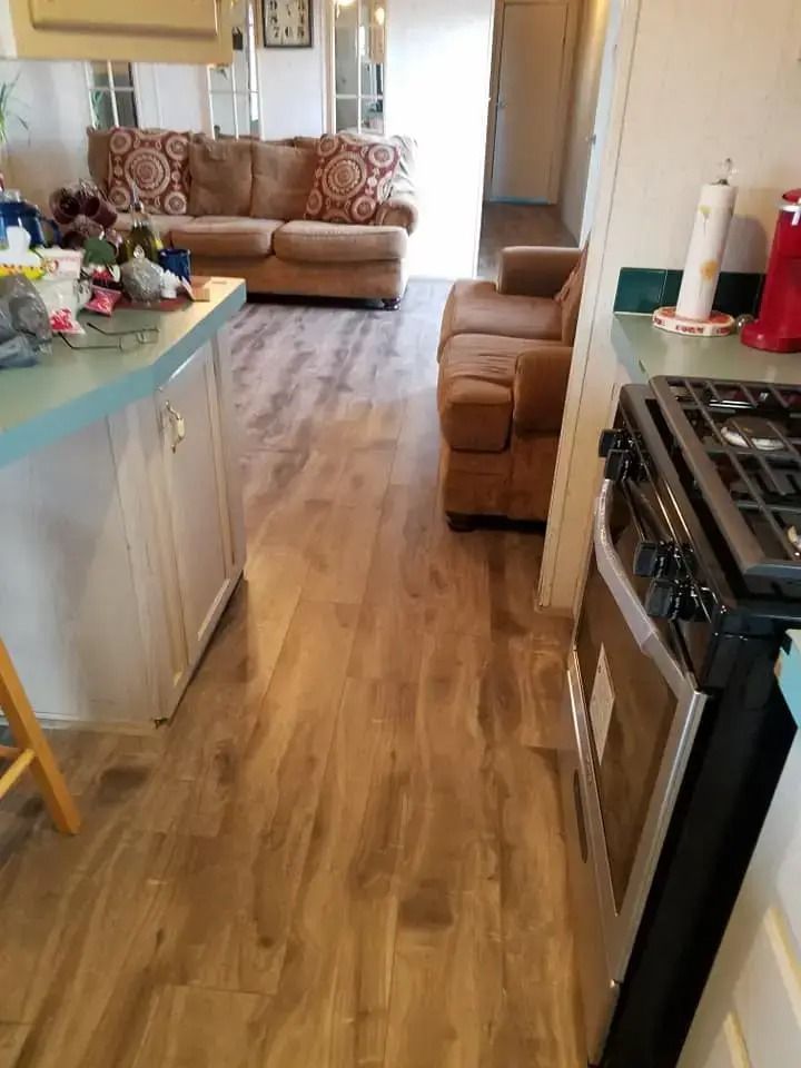 Narrow kitchen with wooden floor, beige sofa, and gas stove in a small open living area