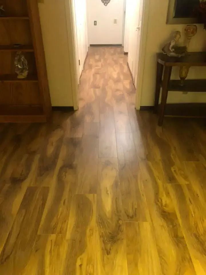 Wood-look hallway leading to a doorway, with wood flooring and small tables on both sides.
