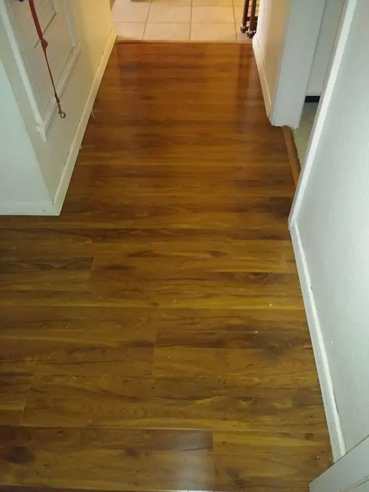 Narrow hallway with wood laminate flooring and white walls leading to a tiled room.