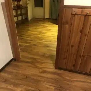 Wooden-floored hallway with a rustic cabinet and shelving at the far end, lit warmly.