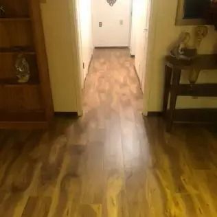 Wooden hallway with polished floors, leading to a bright doorway and small side tables on both sides.