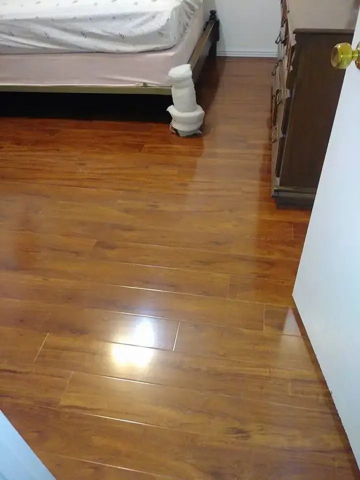 Wooden bedroom floor beside a bed and dresser, with bright light reflecting on the floor.