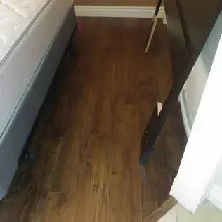 Narrow room with wood flooring, bed on left, and a tilted board leaning against the right wall.
