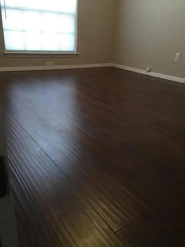Empty room with dark hardwood floors, beige walls, and a bright window.