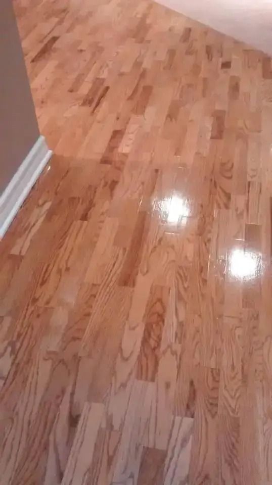 Glossy hardwood floor in a hallway with white baseboards and beige walls