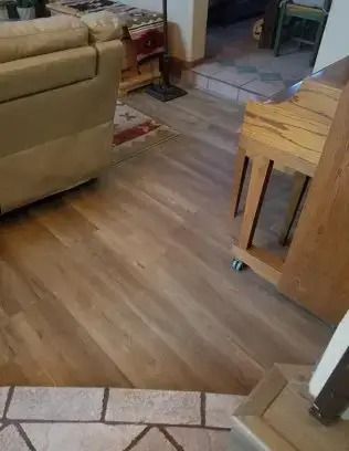 Living room with wood floor, beige sofa, wooden table, and tiled entryway.
