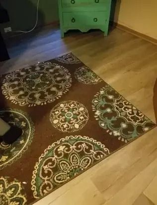 Brown patterned rug on light wood floor beside a green dresser in a room