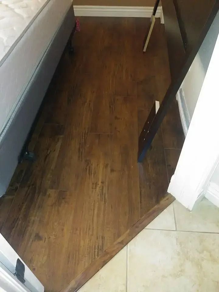 Narrow wooden hallway between furniture, with tiled floor at the entrance and a white wall on the right.