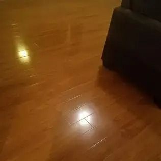 Shiny wooden floor with a dark couch edge on the right and a bright light reflection on the floor.