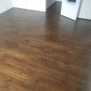 Empty room with brown wood flooring and white walls, viewed toward an open doorway.