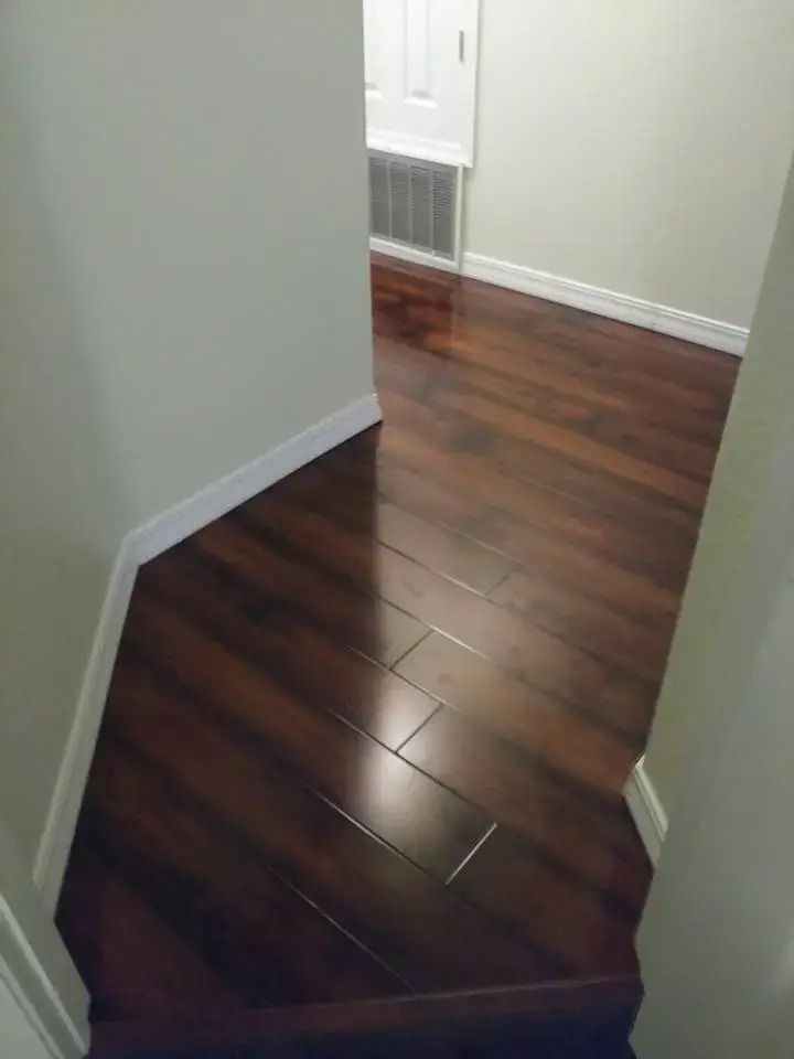 Hallway with dark wood flooring and white walls, showing a narrow turn near a vented door.