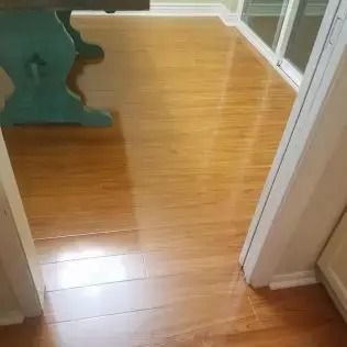 Shiny hardwood floor in a room, with a green table on the left and a doorway to the right.