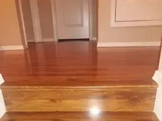 Wooden floor with a small step up into an empty hallway with beige walls and doorways.